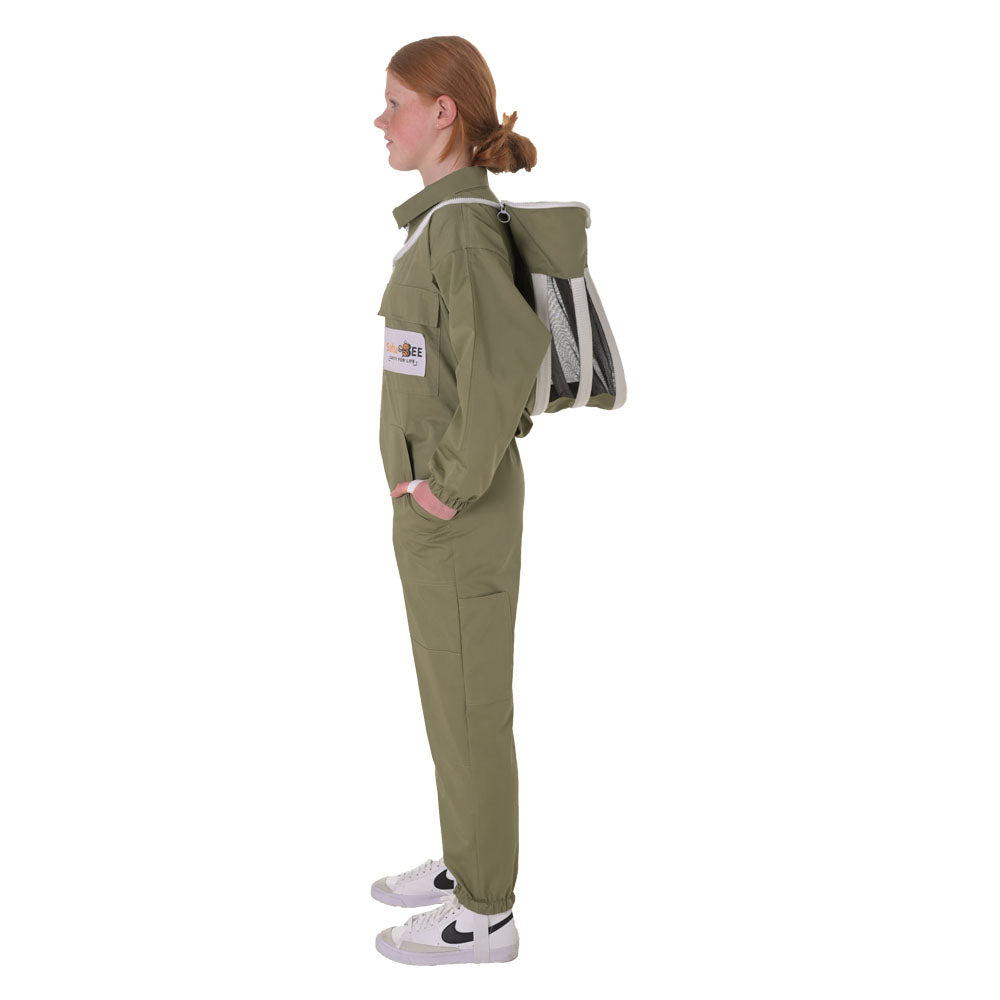 A kid in profile wearing an olive green jumpsuit and a gray-and-white backpack, standing against a plain white background.